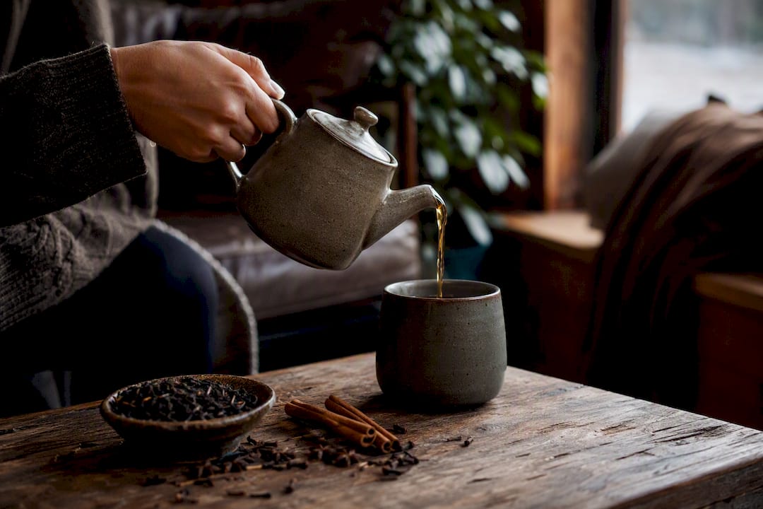 Hands pouring hot spiced winter tea into rustic mug